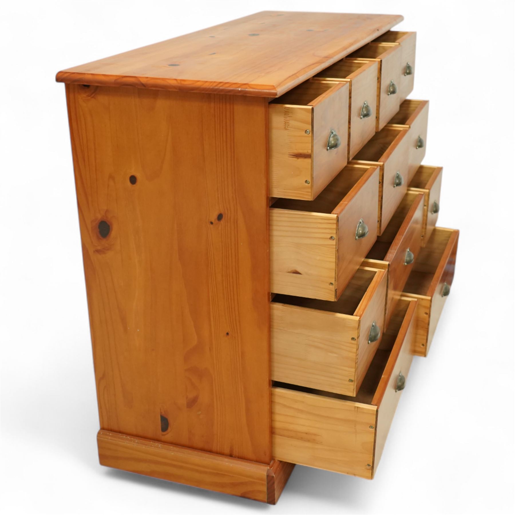 Late 20th century pine merchants chest, rectangular top over an arrangement of twelve small and four larger drawers, each with recessed panel facias and brass cup handles, plinth base
