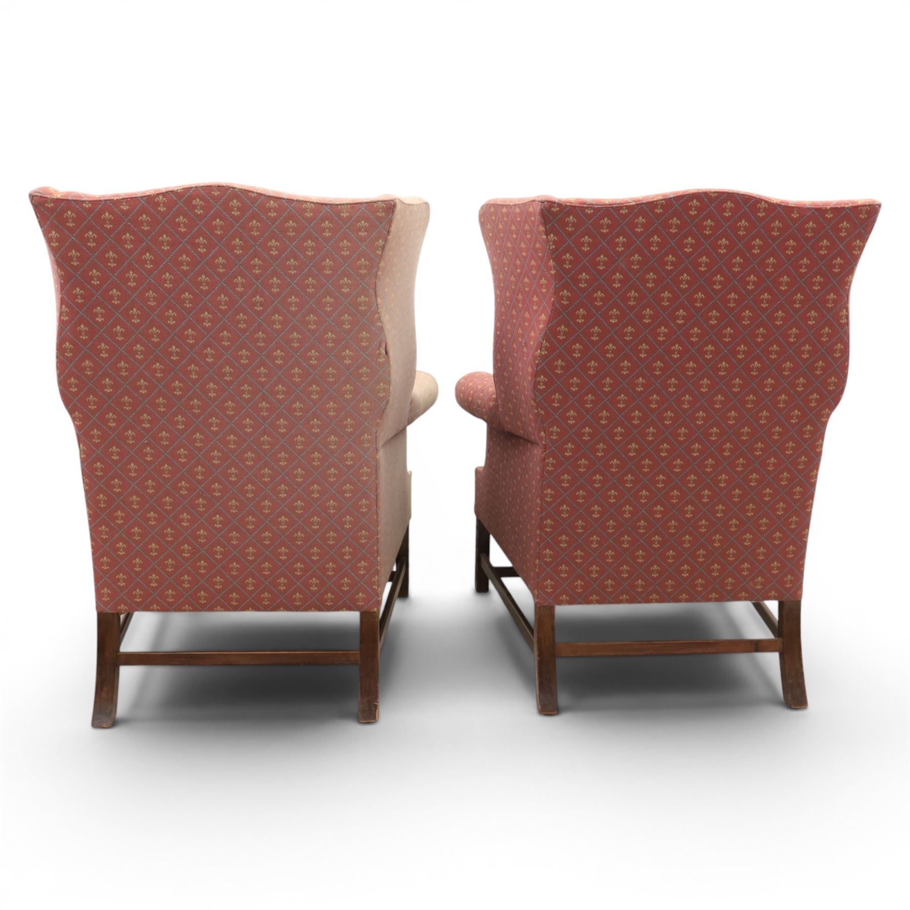 Georgian design wingback armchairs, the high backs flanked by shaped wings over padded scroll arms, upholstered in burgundy and gilt fleur-de-lys patterned fabric, loose cushion seats, raised on square tapering front supports