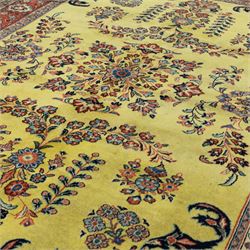 Persian Sarough hand-knotted carpet, golden yellow ground, with an all-over floral design centred by a small floral motif, the field decorated with mirrored flowering sprays, scrolling vines and dark navy foliate corner motifs, enclosed by a terracotta border with repeating flowerheads and palmettes, flanked by narrow guard stripes, with cotton fringes