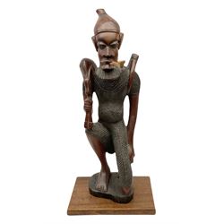 Large carved African figure of a man on one knee, supporting a dead animal over his shoulder and a weapon to his back, smoking a pipe in his mouth, upon rectangular base, H67cm