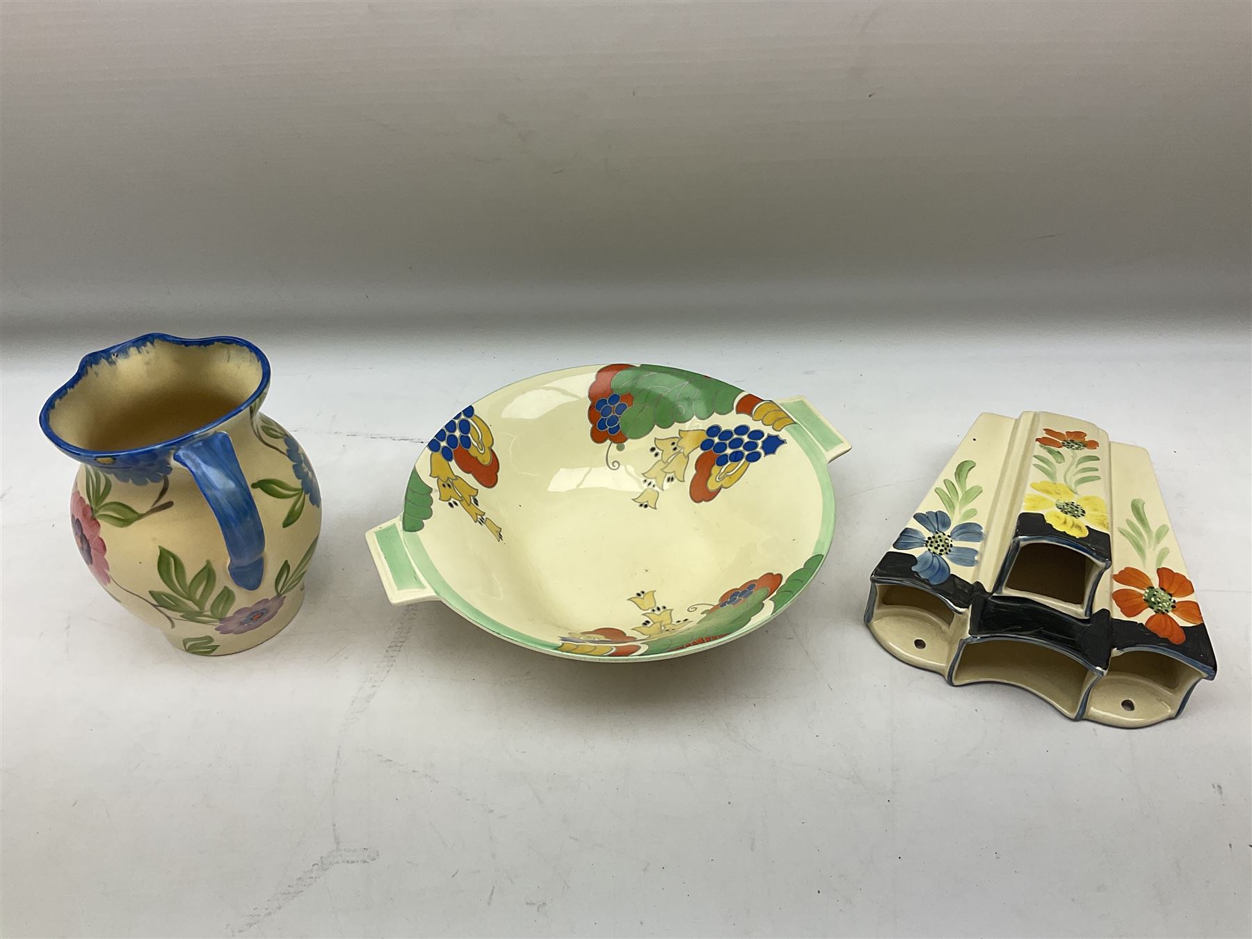 Group of Art Deco ceramics, comprising Wadeheath jug painted in spiralled bands of blue, orange, yellow and brown, shape no. 707784, Royal Doulton Caprice pattern twin handled bowl, no. D5358, Arthur Wood wall pocket of typical stylised fan form with painted floral decoration, Arthur Wood vase of cornucopia form with red and grey floral decoration, Wadeheath jug of ribbed form with stylised handle, and two Hancock's Ivory Ware jugs, tallest example H26cm