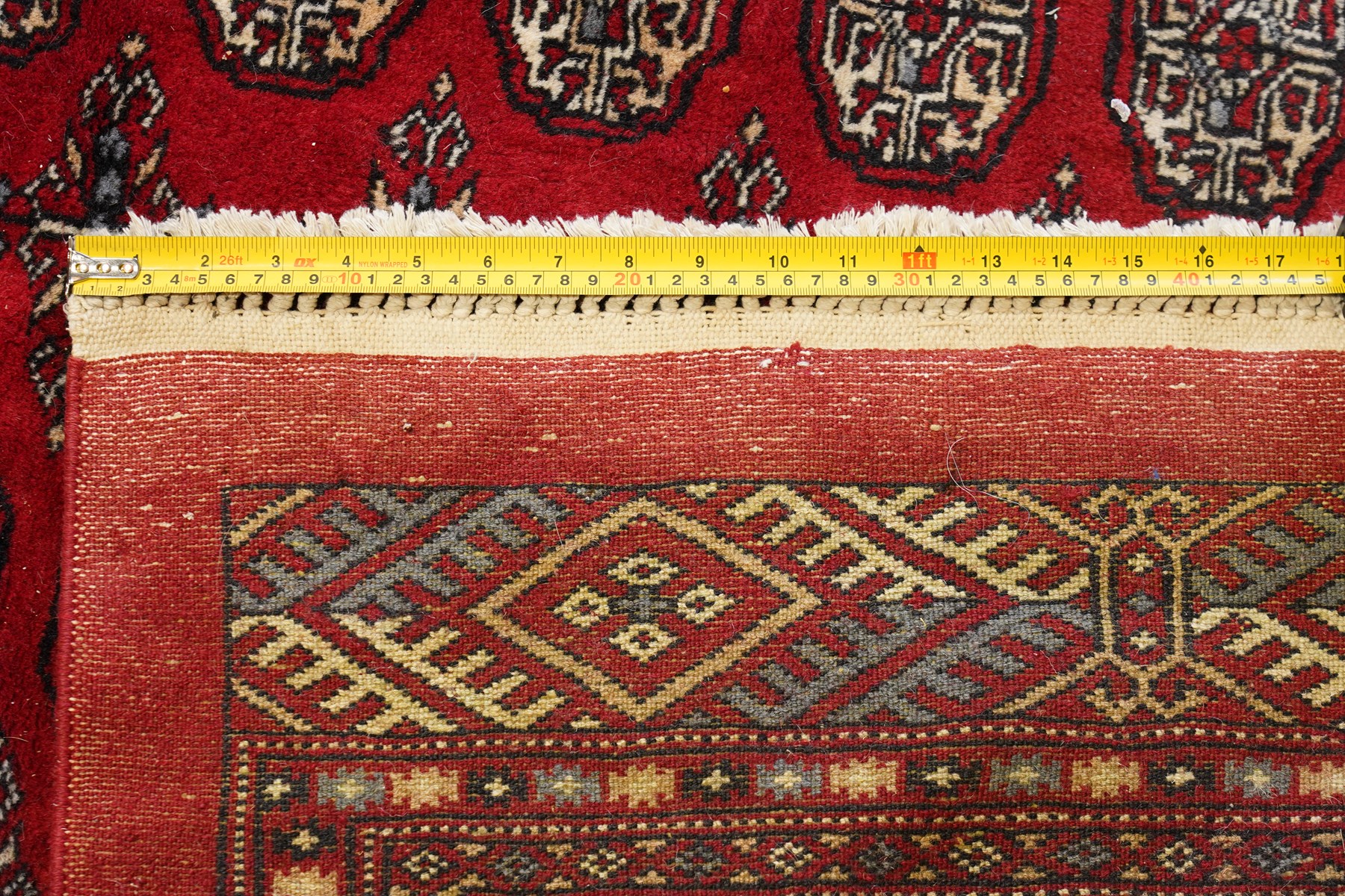 Large crimson ground Afghan Bokhara carpet, the field decorated with repeating Gul and geometric motifs, the multiple guard stripes with further geometric decoration