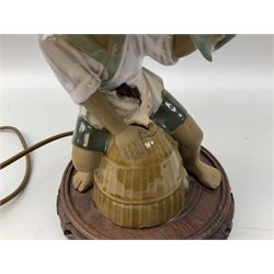 Japanese ceramic figural table lamp modelled as a fisherman with catch upon barrel, upon circular carved wood plinth with tassel shade, H50cm