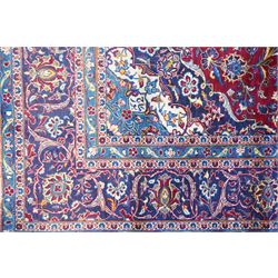 Central Persian Kashan hand-knotted carpet, crimson field with a central elaborate cusped medallion surrounded by elegant scrolling floral vine design incorporating stylized palmettes, rosettes and foliate sprays and similarly decorated spandrels enclosed by a dark indigo main border of floral arabesques between multiple guard stripes, cotton fringe ends 