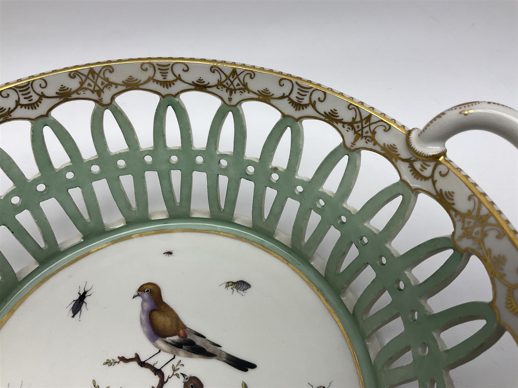 Pair of 19th century German openwork chestnut baskets, with twin handles and scrolling gilt border and star rim, painted to the centre with birds and insects, D22cm 