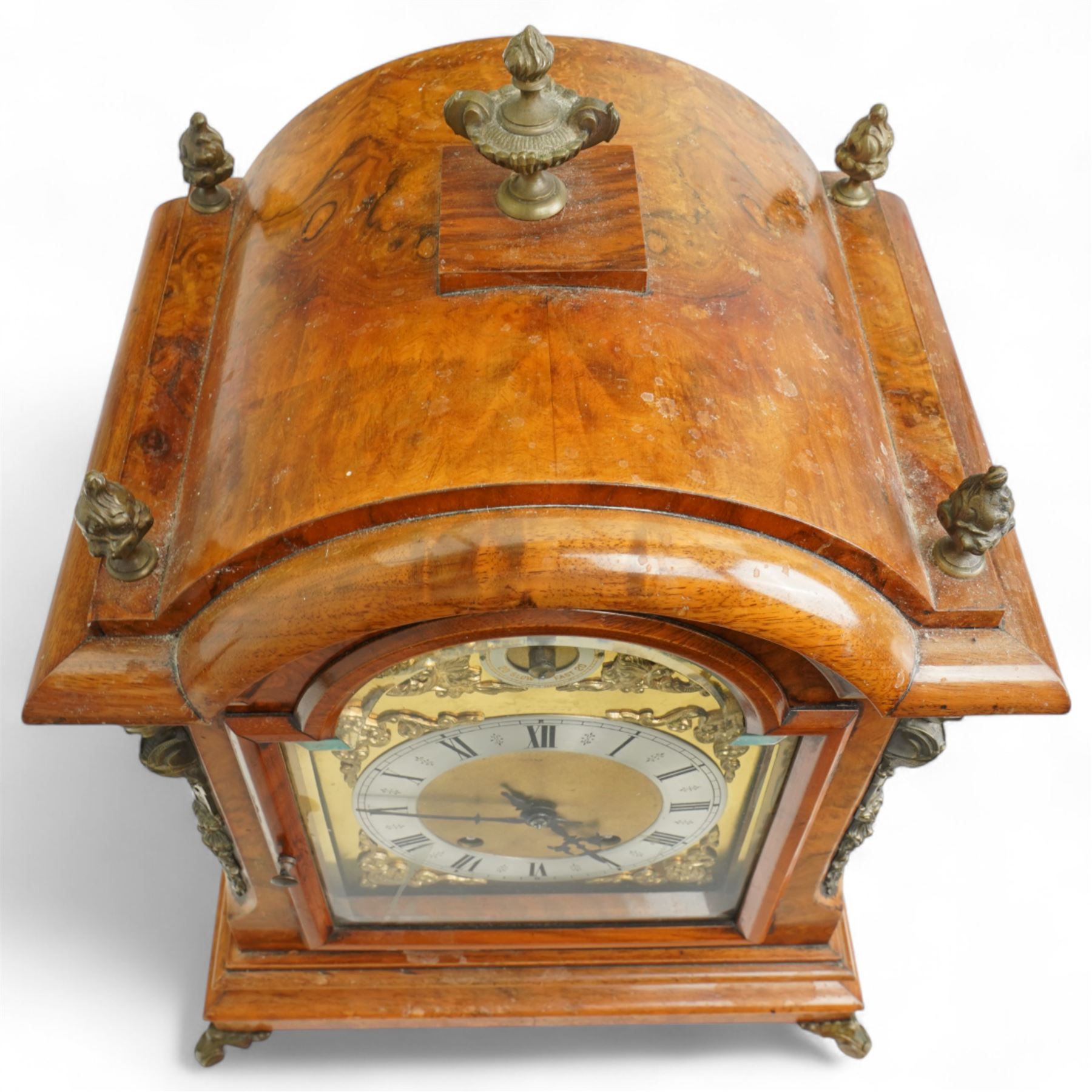 German-early 20th century mantle clock c1910, in a walnut case with a break arch top and decorative cast brass finials, brass silk backed sound frets to the sides and a glazed break-arch door flanked by a pair of cast brass caryatid, on a dee ogee moulded plinth and raised on splayed paw feet, brass dial with cast spandrels and a matted dial centre, silvered chapter ring with Roman numerals, gothic steel hands and a conforming pendulum regulation dial to the arch, two train going barrel movement with rack striking, sounding the quarters on two gongs and the hour on one, With Pendulum and key.
