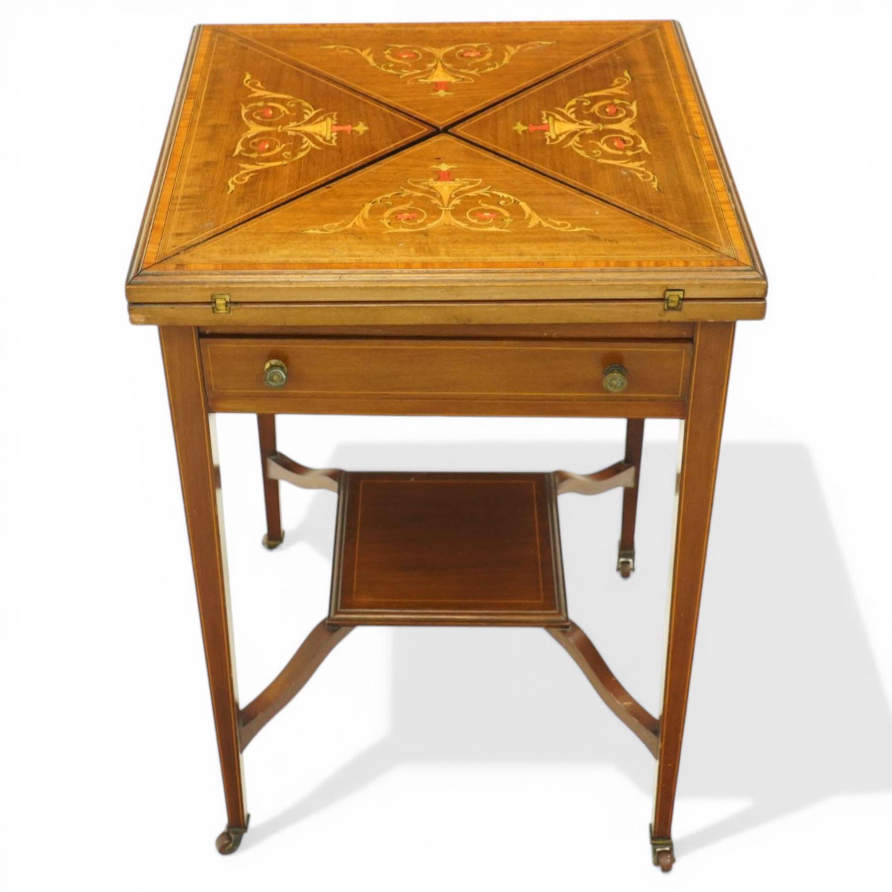 Edwardian inlaid mahogany envelope table, square top with triangular leaves revealing a baized lined interior and wells, raised on tapering supports united by an under tier, terminating in brass castors