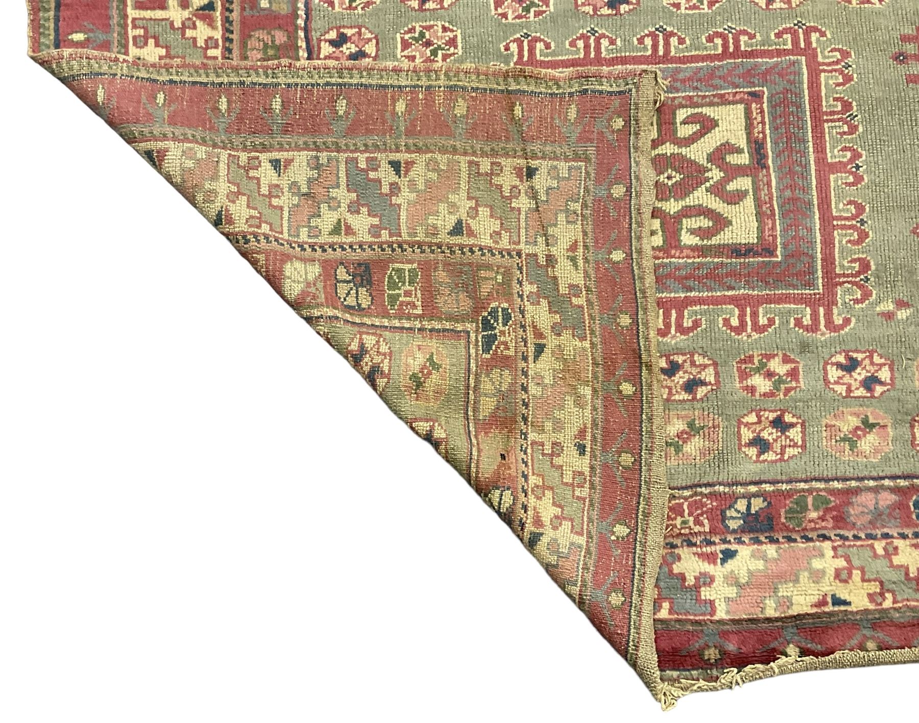 Turkish deep pink and green ground carpet, the square field with hooked borders surrounded by geometric motifs, multi-band border with overall geometric designs 