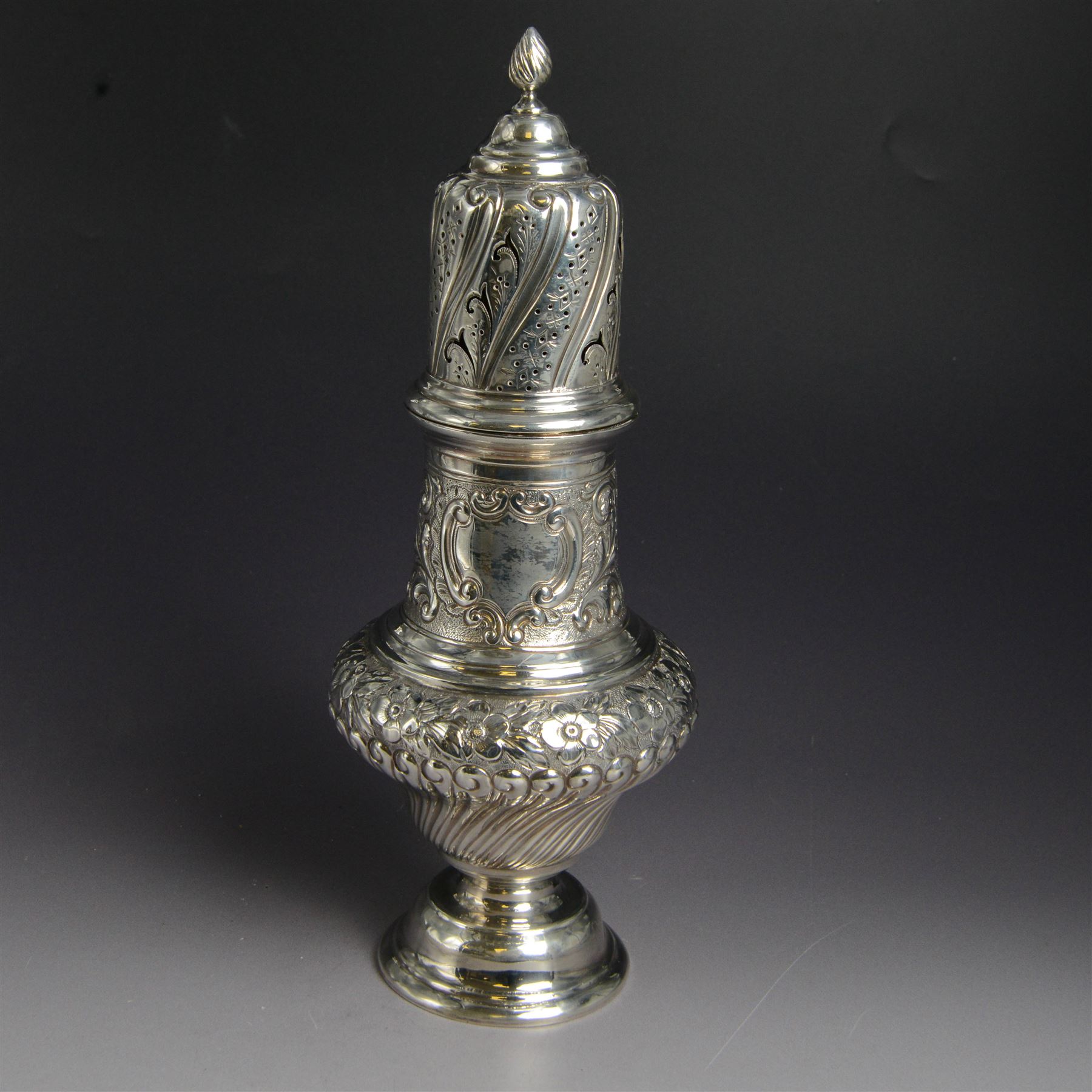Victorian silver sugar caster, of bellied urn form, embossed with floral and foliate motifs, with two vacant cartouche, upon a domed stepped circular foot, with pierced removable cover with flambe finial, hallmarked Marston & Bayliss, Chester 1900, H25cm