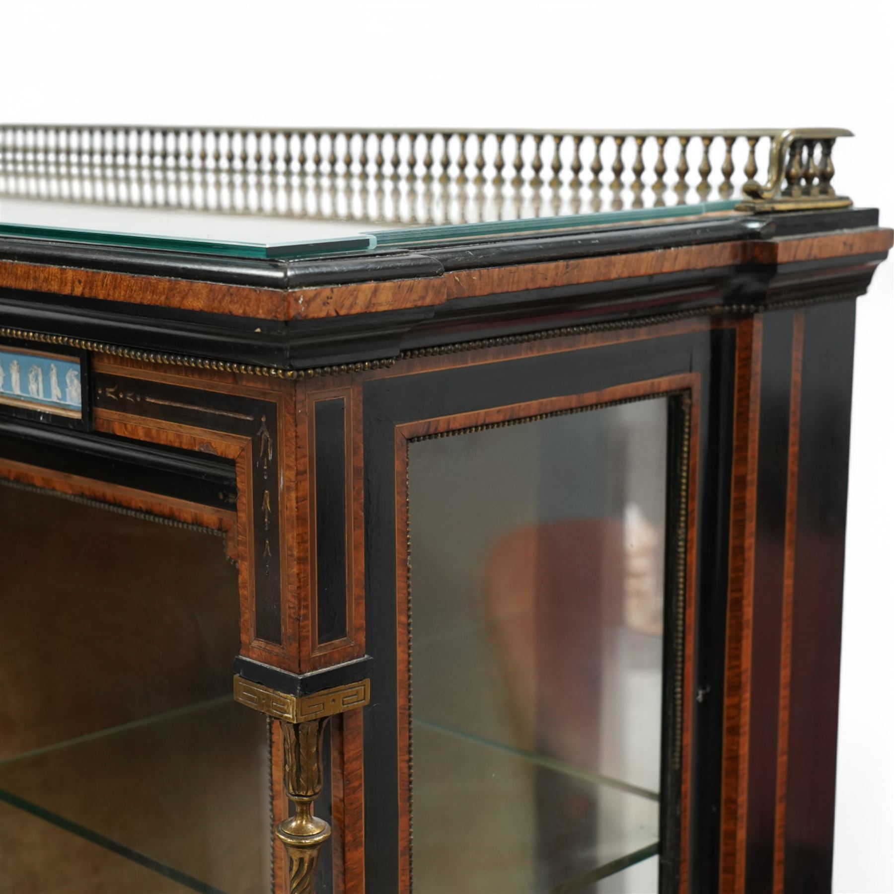 Victorian amboyna and ebonised credenza with glass top, the freeze fitted with two Wedgewood plaques and brass beading above crossbanded arched glazed mirror door flanked by two glazed cabinet doors with two removable glass shelves between four gilt brass reeded floral columns, supported on bun style feet
