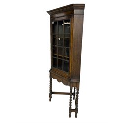 Early to mid-20th century oak corner display cabinet, projecting cornice over astragal glazed door, on spiral turned supports joined by stretchers
