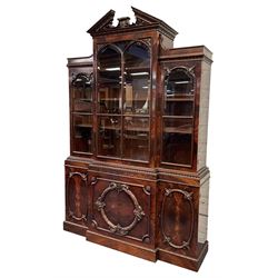 Large Georgian style mahogany breakfront bookcase, sloped pediment carved with foliage, the top section enclosed by astragal bevel glazed doors, the lower section enclosed by three cupboard doors decorated trailing flower head and cartouche mounts, on plinth base 