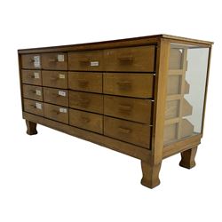 Early 20th century oak framed haberdashery shop counter, veneered top with glazed front and sides, fitted with sixteen graduating drawers with oak fronts and handles, raised on shaped supports