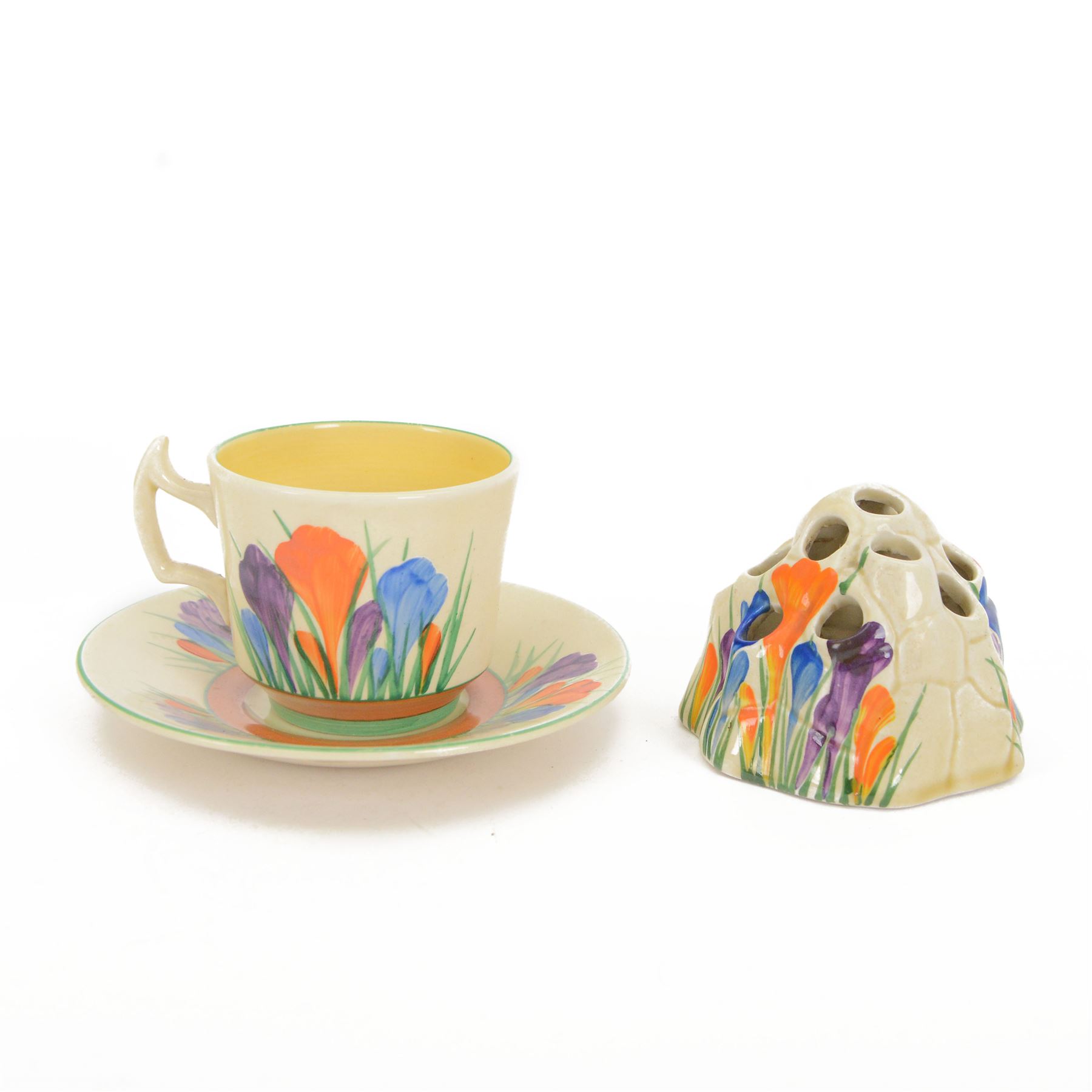 Royal Staffordshire Crocus by Clarice Cliff teacup and saucer, with printed mark beneath, together with a Clarice Cliff Crocus pattern flower frog, with printed mark beneath, cup H6cm