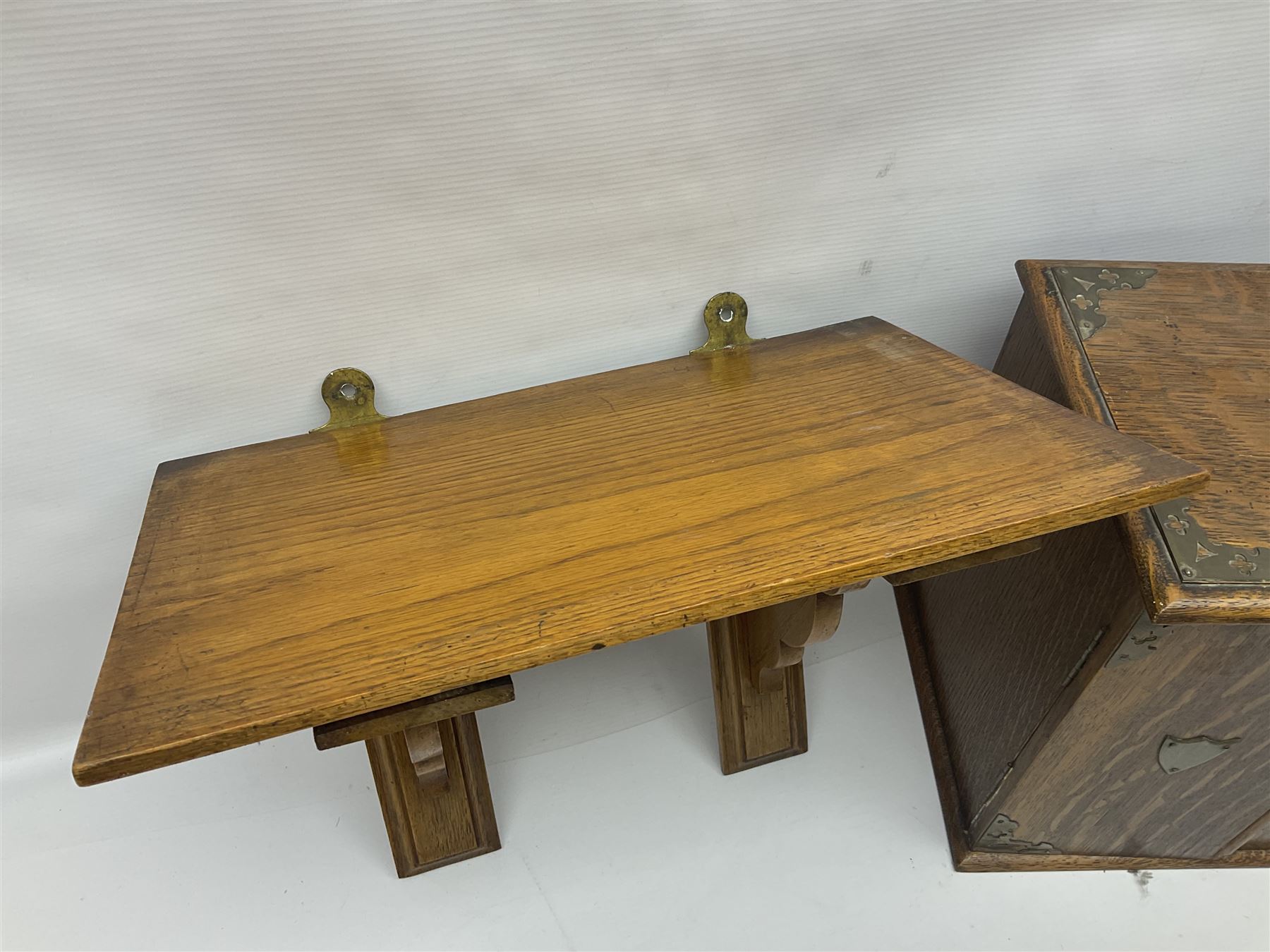 Early 20th century oak smokers cabinet, with brass shield shaped mounts, opening to reveal a compartmentalised interior with three drawers, pipe rack and tobacco jar, together with a small wooden shelf, smokers cabinet H28.5cm