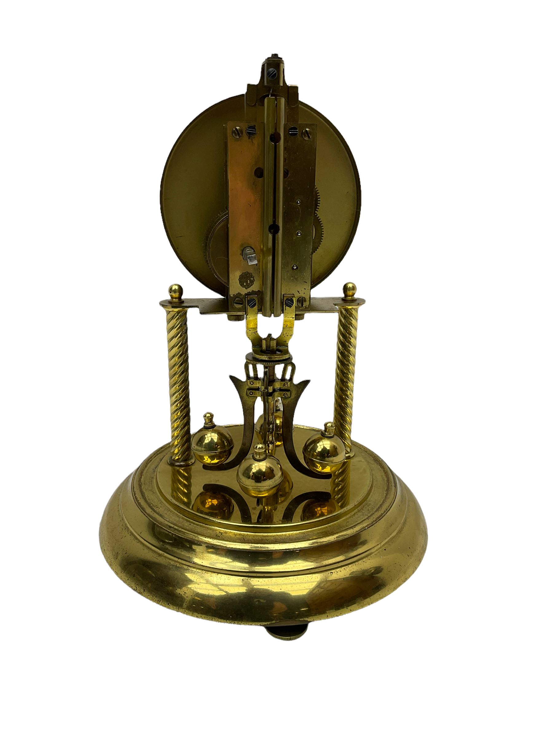 A mid-20th century “Bentima” 400-day anniversary torsion clock with a 7” circular brass base and unenclosed movement supported on two twisted columns, with a white dial gilt numerals and baton hands, four-ball rotary pendulum and glass dome. 

