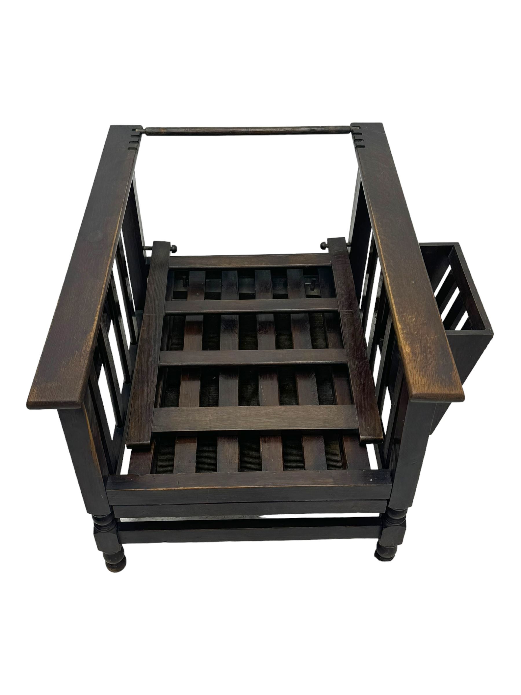 Late Victorian oak steamer chair, adjustable slatted backrest with grooved crest rail, wide armrests extending to a sliding adjustable footrest, open frame sides with vertical slats, side magazine rack and collapsible table, raised on turned front supports