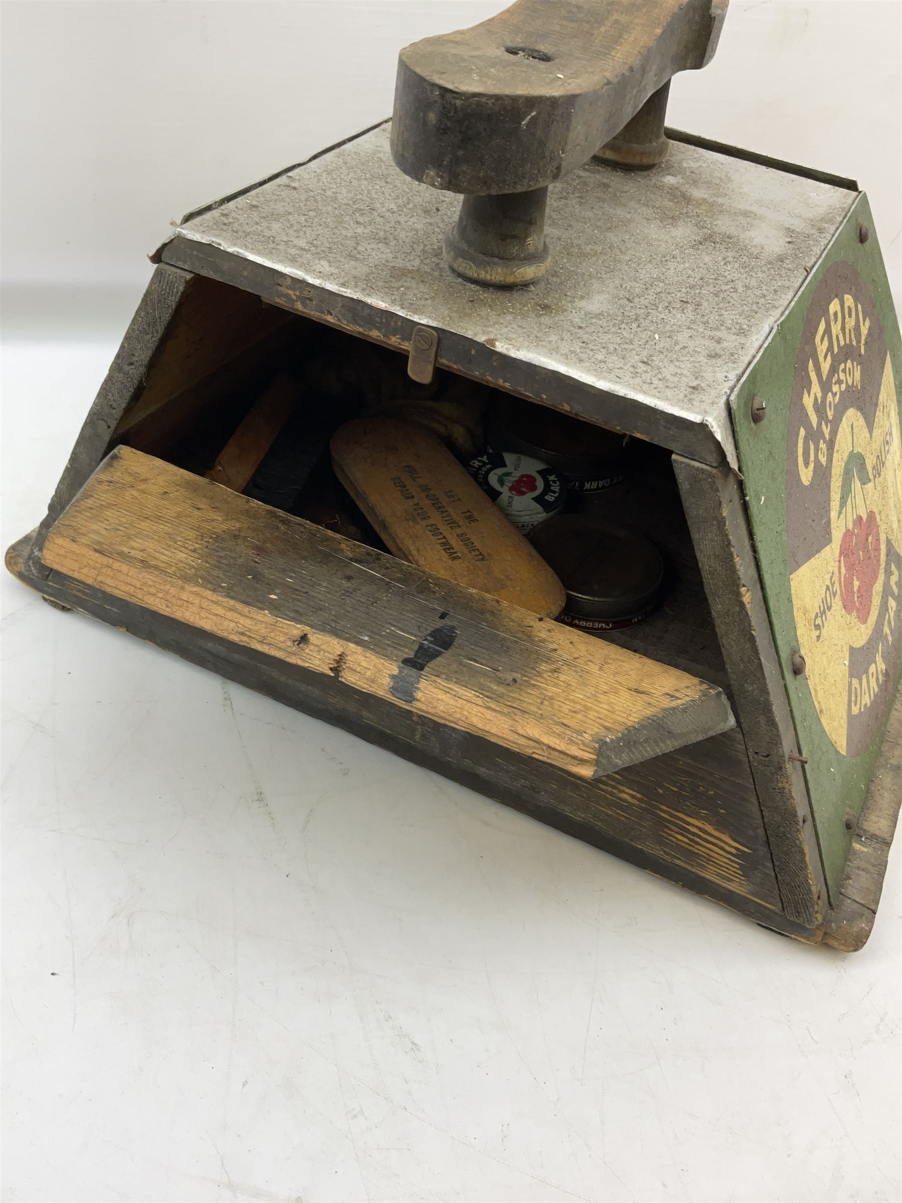 Cherry Blossom Shoe Polish shoe shine box, of sloping form, with three pictorial enamel panels advertising dark tan, black and light tan polishes, the reverse with a hinged compartment, the top mounted with a handle and foot rest in the form of a shoe sole, H29cm W42cm D33cm