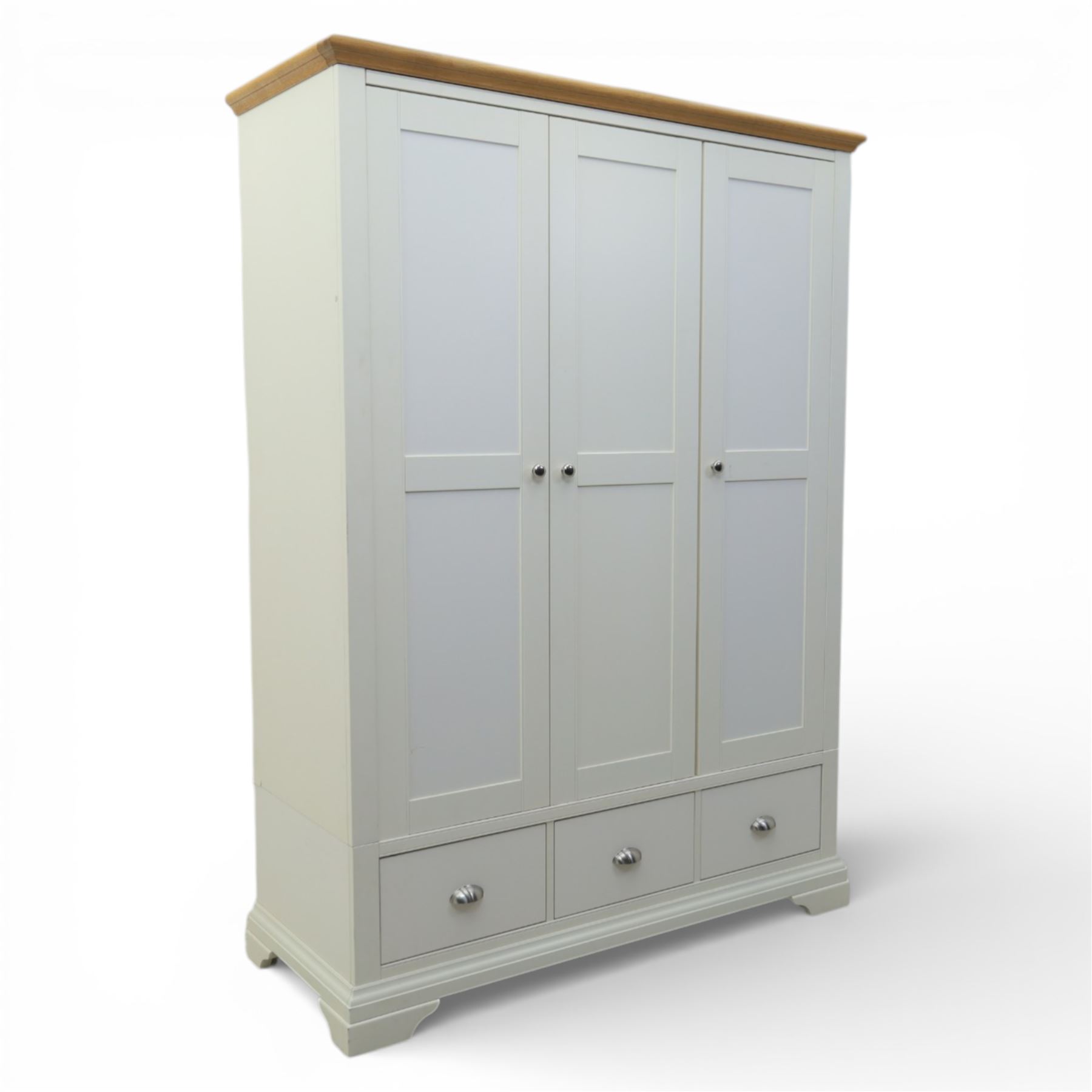 Modern triple wardrobe in white finish with oak moulded top enclosed by three doors with three drawers to base, with metal cup handles raised on bracket feet
