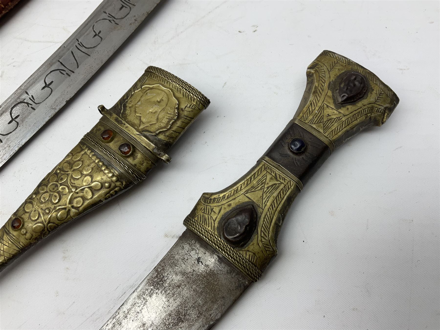 Near pair of African Moroccan Berber tribal Shula daggers each with engraved 39cm curving fullered steel blade, carved and inlaid horn grip and leather covered scabbard L57cm overall; kindjal style dagger with brass covered and jewelled grip and scabbard; another Eastern dagger with leather covered grip and scabbard; and a large Eastern knife with animal hide scabbard (5)