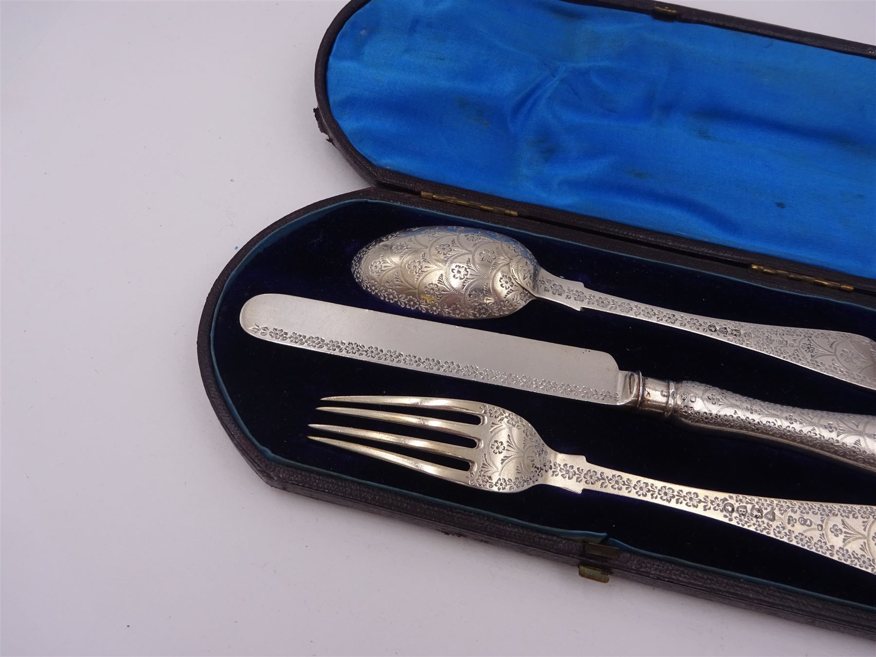 Victorian silver cutlery set, comprising knife, fork and spoon, all profusely engraved with flower heads, each with initials terminals, hallmarked Chawner & Co Birmingham 1877, contained within tooled leather, velvet and silk lined fitted case