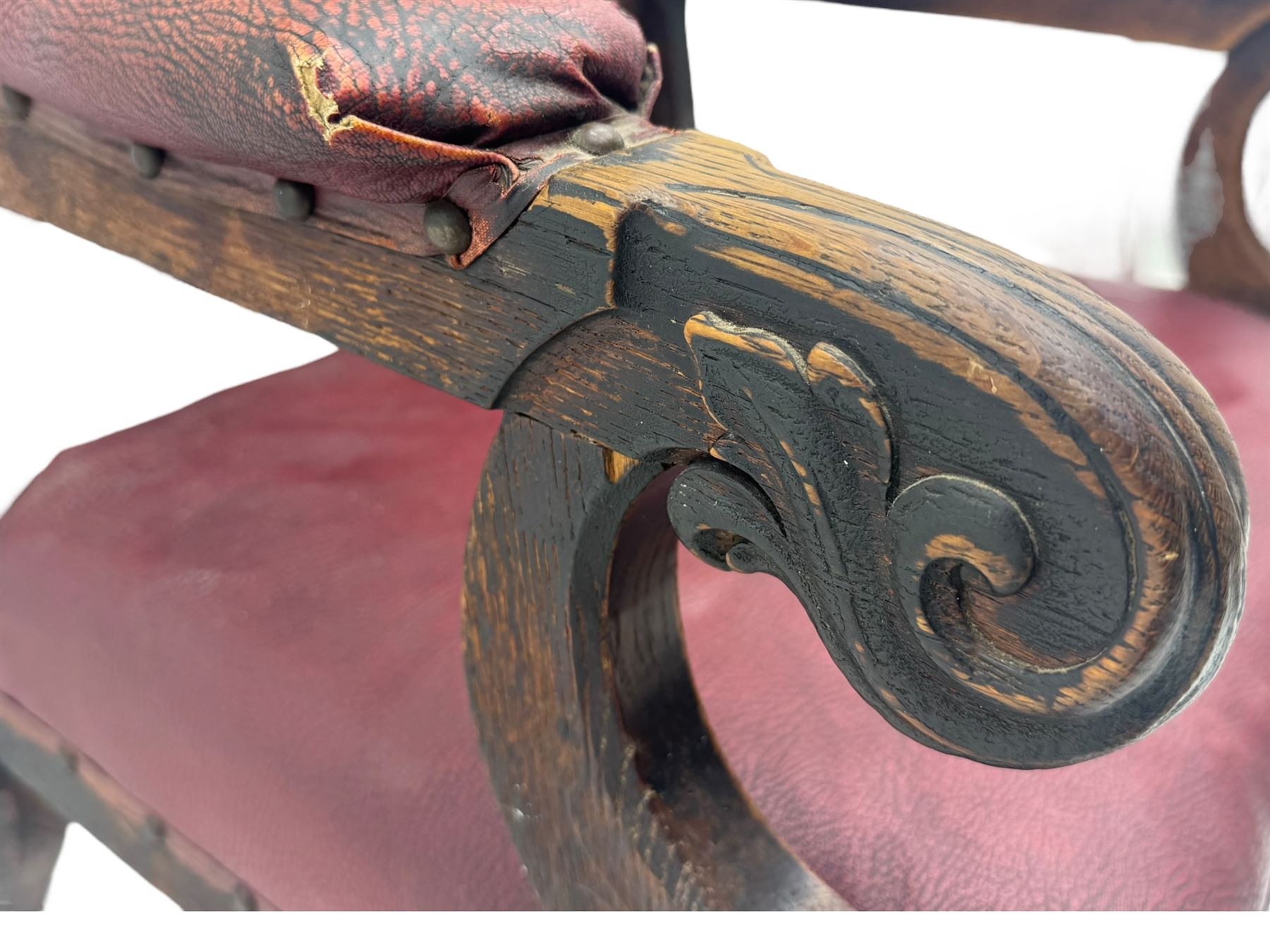 Late Victorian Gothic-revival armchair, arched crest rail carved with tracery and trefoil detail, padded circular back and seat, brass studded burgundy leather upholstery, shaped armrests with scrolled terminals, on square tapering supports