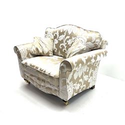 Snuggler armchair upholstered in a pale gold ground fabric with floral pattern, shaped cresting rail, scrolling arms