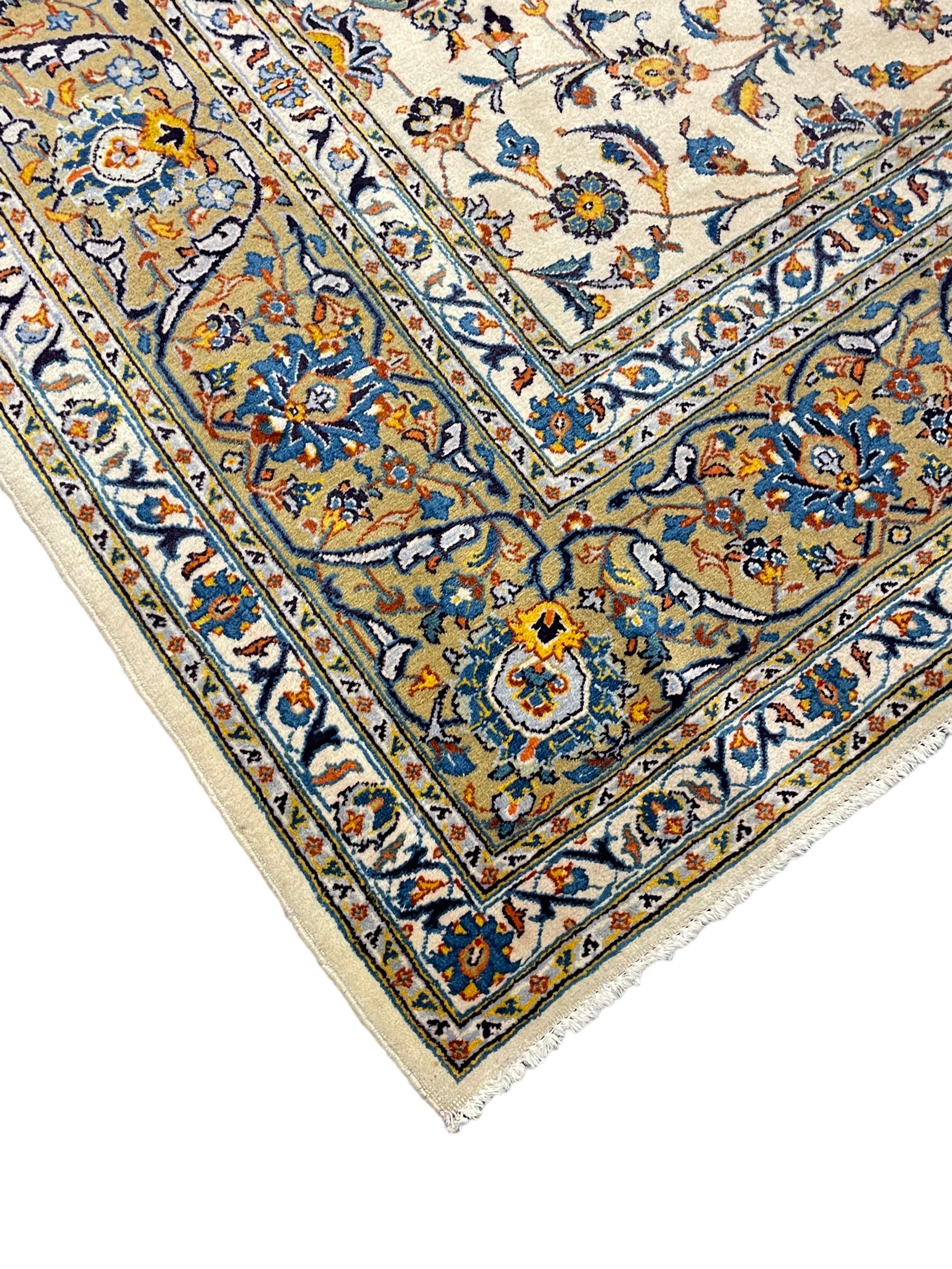 Persian Kashan ivory ground carpet, the field decorated with trailing foliate branches and stylised flower head motifs, guarded border with repeating design decorated with scrolling leafy branch and plant motifs 