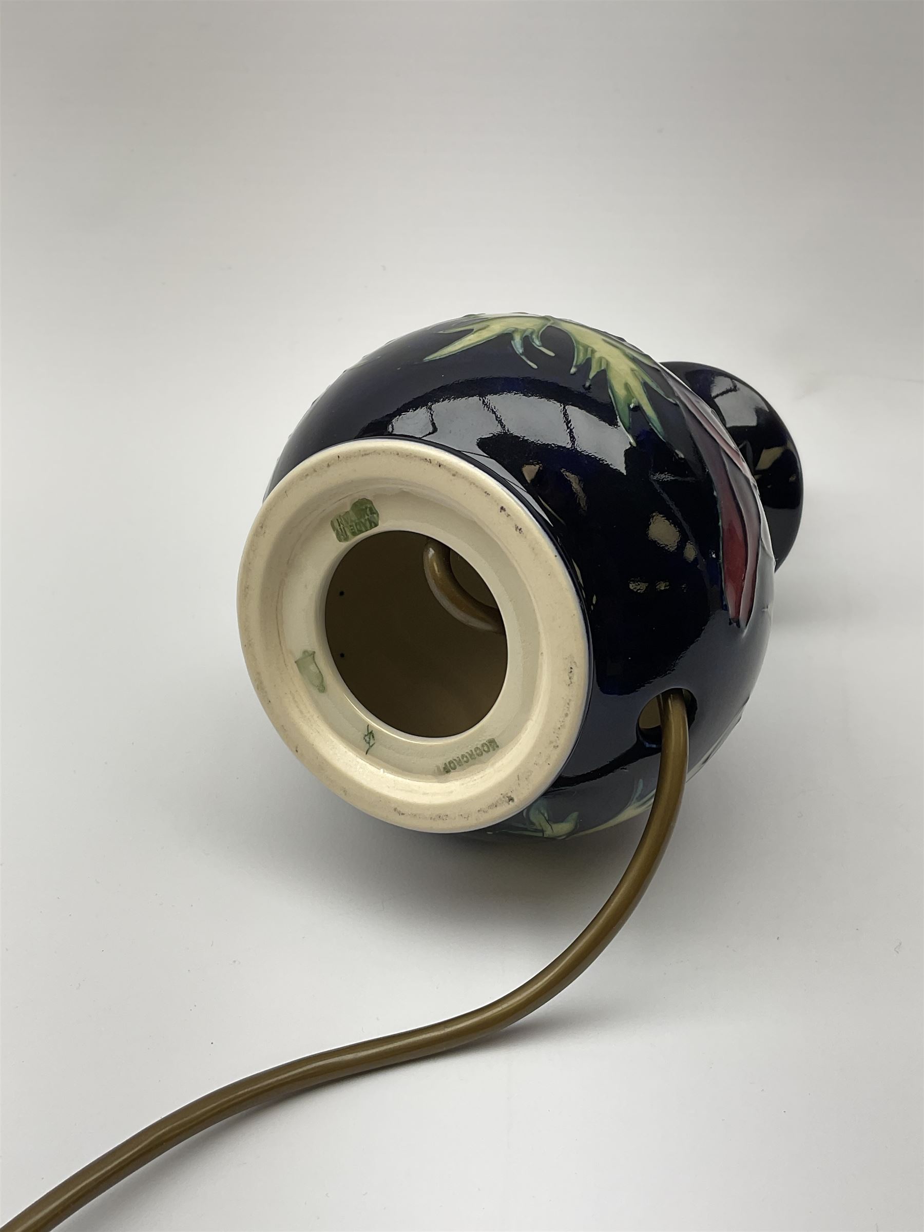 A Moorcroft table lamp, of baluster form, decorated in the Anemone pattern upon a dark blue ground, with impressed marks beneath, with accompanying cream shade with piped detail, overall H38.5cm.