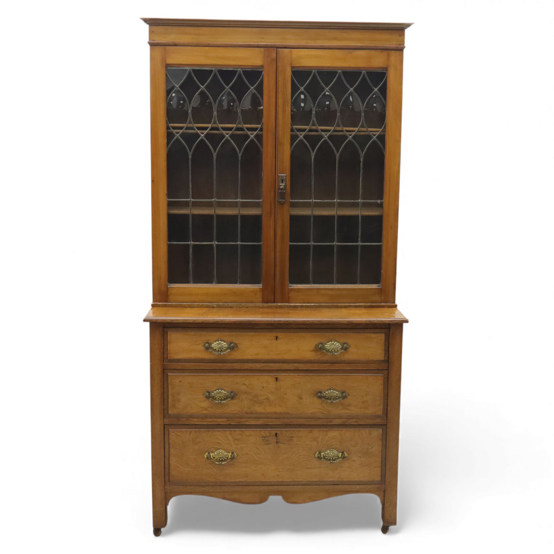 20th century wooden bookcase cabinet, fitted with a pair of leaded glass panel doors opening to adjustable shelves, the base top and front veneered in richly figured walnut, contrasted with solid oak panelled sides and shaped lower frieze, terminating in castors