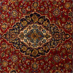 Central Persian Kashan hand-knotted carpet, crimson red field with a central shaped palmette medallion with pendants, filled with dense scrolling and floral motifs, enclosed by a navy blue border decorated with palmettes and meandering vine scrolls, flanked by multiple guard stripes, with cotton fringe ends 