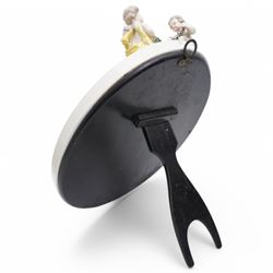 Sitzendorf oval table mirror with two cherubs holding a floral garland above foliage and insects etc on easel stand 40cm x 31cm