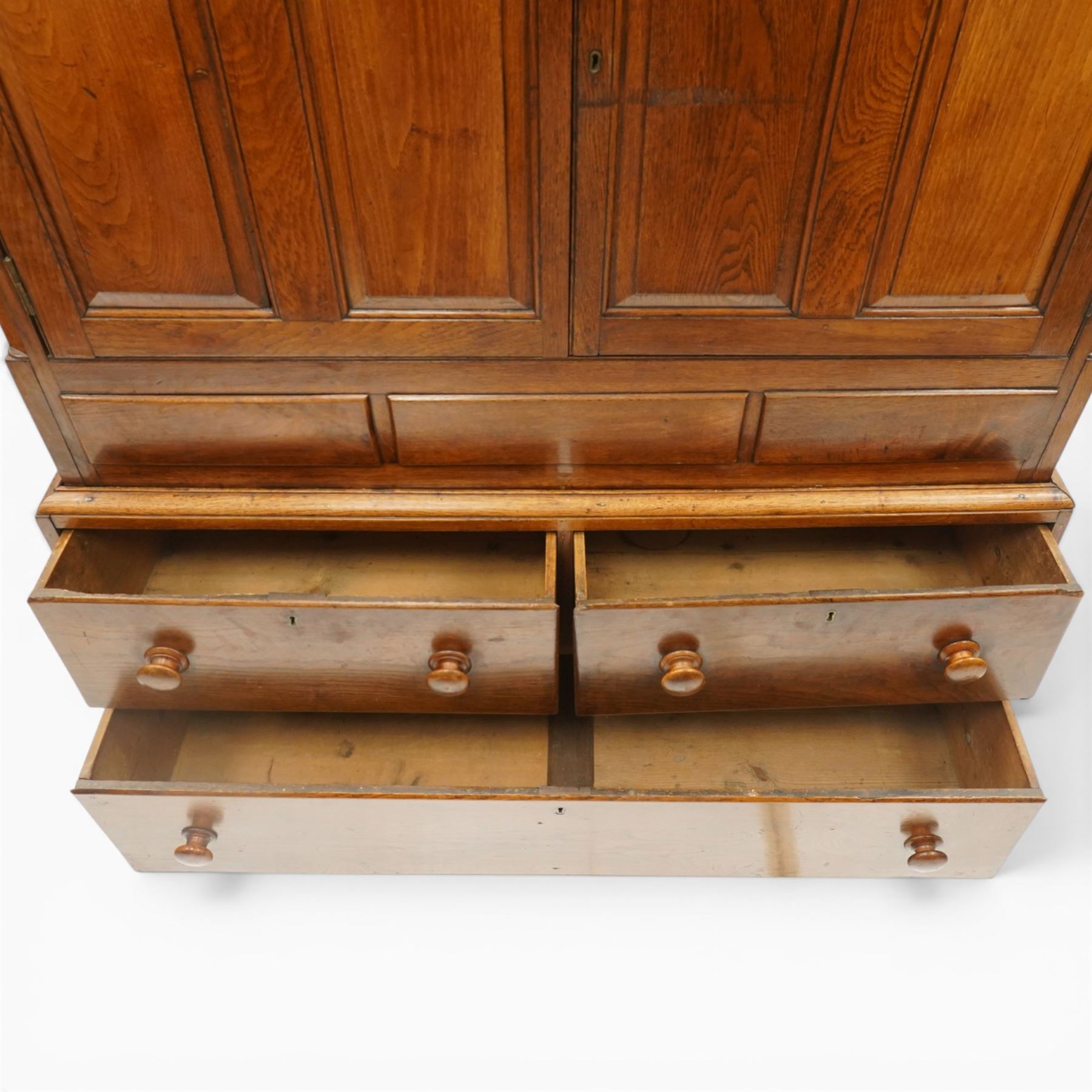 18th century oak larder cupboard, projecting moulded cornice over two panelled doors with shaped arched fielded panels, three short dummy drawers above base fitted with two short and one long drawer, turned handles, on bracket feet