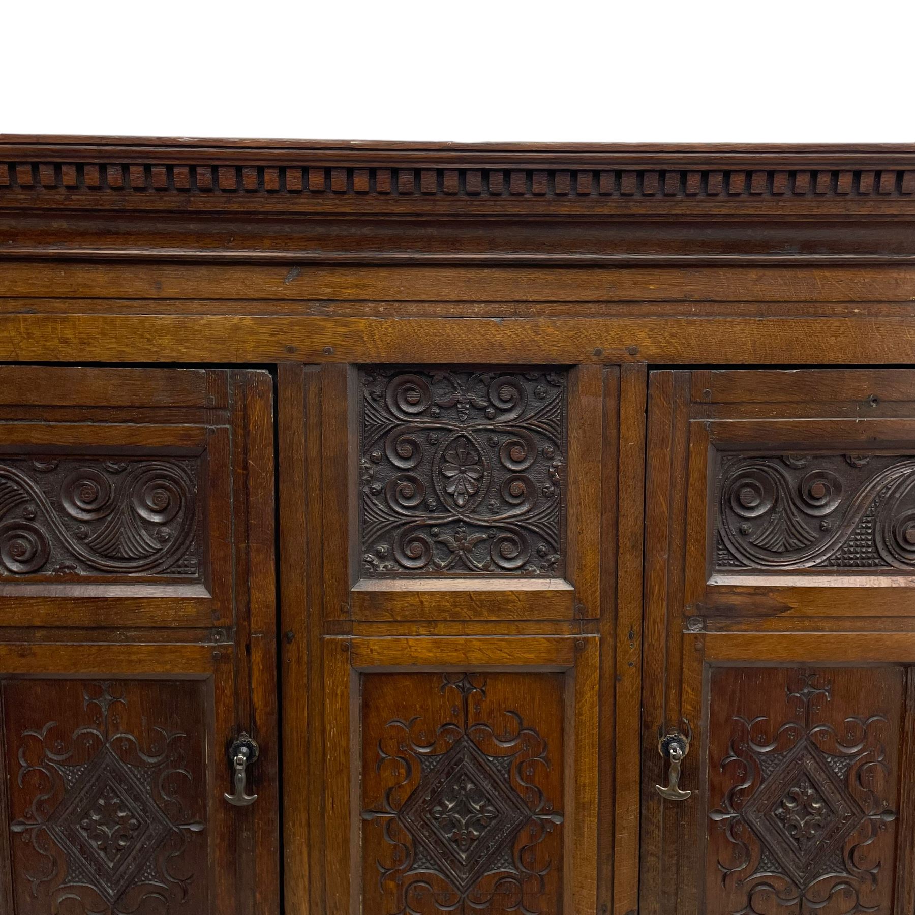 Large 18th century and later oak livery cupboard, projecting moulded and dentil cornice, sunken fillet moulded frame, triple vertical panelled central upright, enclosed by two doors each with five panels, the top row of panels carved with stylised scrolls, the lower panels carved with foliate lozenges, on shaped bracketed skirt base 