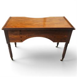 In the manner of Gillows - Regency period mahogany kneehole dressing table or writing desk, the shaped rectangular top with raised three-quarter gallery, fitted with central concave frieze drawer flaked by two graduating drawers to each side, each with ebony stringing, raised on turned and reeded supports terminating to brass cups and castors