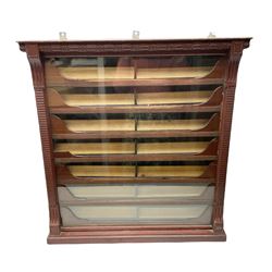 Late Victorian wall mounting cigarette case or display cabinet, the cornice with repeating oval guilloche decoration, ribbed uprights enclosing glazed window, fitted with seven sliding drawers with divisions and mounting blocks, in red finish, inscribed verso. 