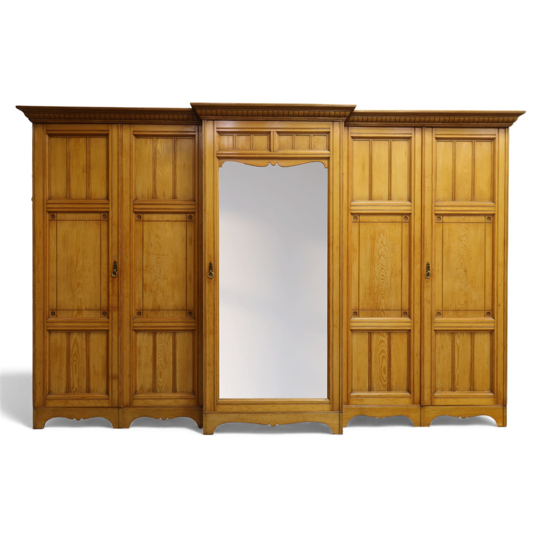 Gothic revival ash breakfront wardrobe in the manner of Charles Bevan, the four fielded panelled doors flanking a central mirrored door, opening to reveal an fitted interior with hanging rails and compartment shelves and drawers, upon a shaped plinth base with bracket cut feet

