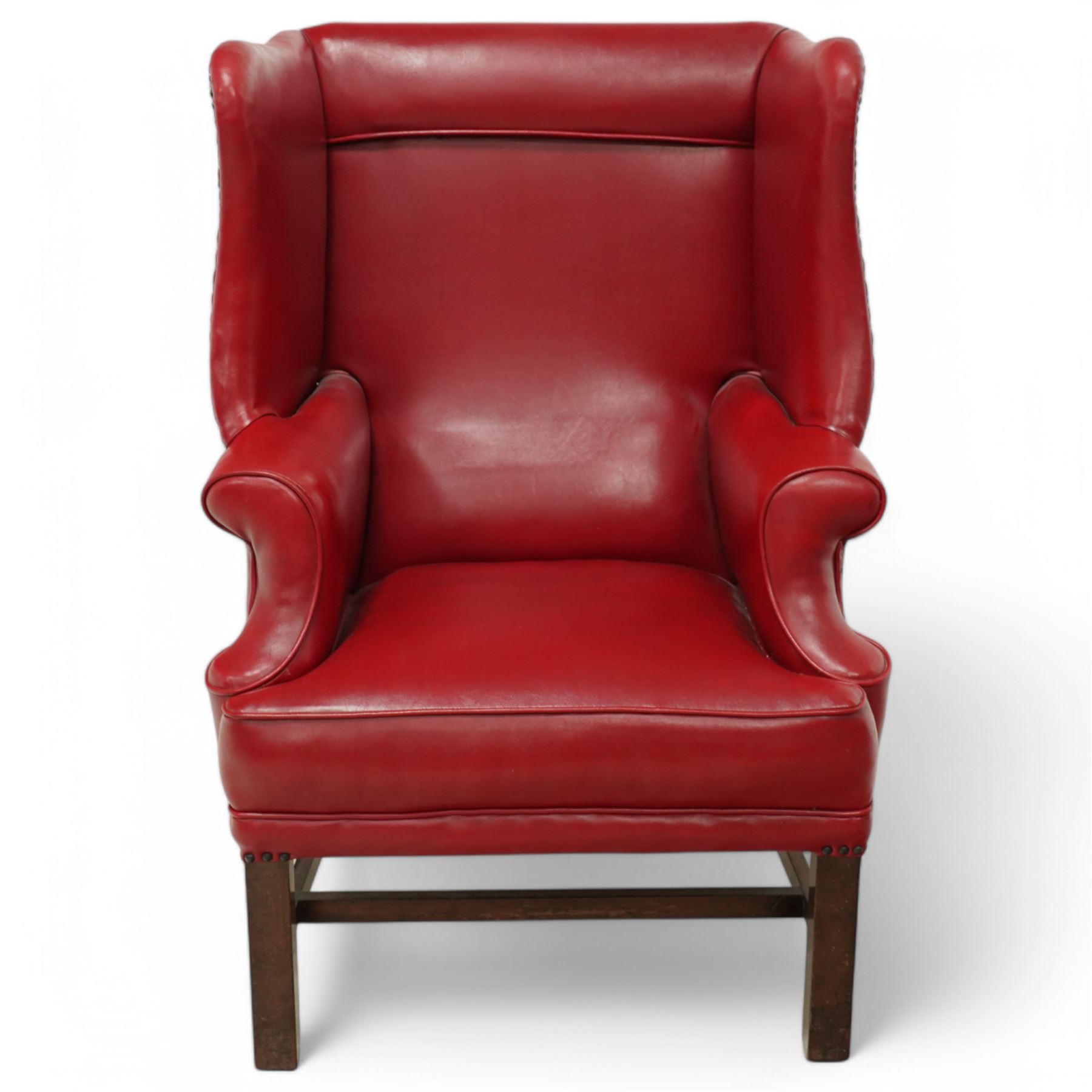 20th century Georgian design mahogany framed wingback armchair upholstered in red leather, shaped back flanked by winged sides and down-swept arms raised on squared legs 