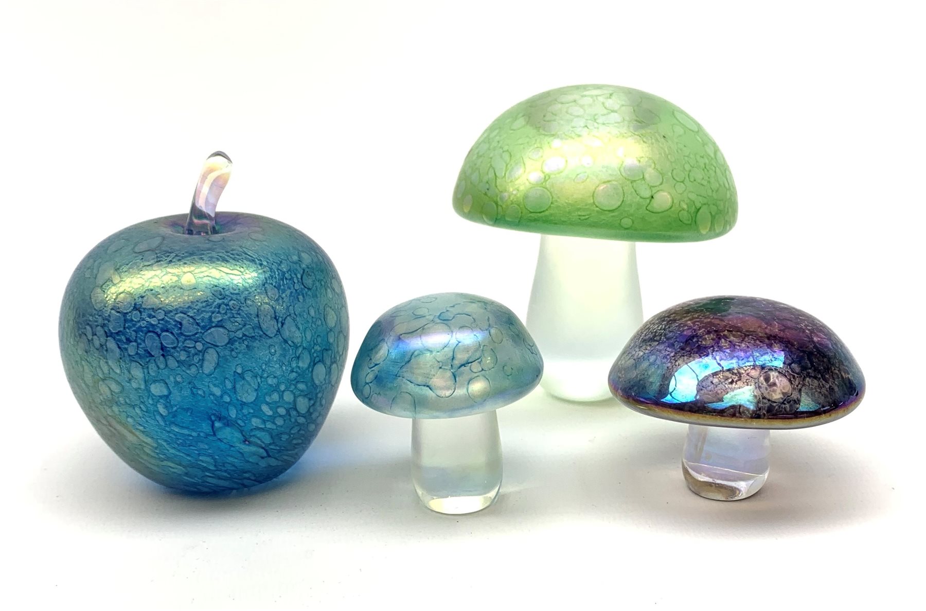 Three John Ditchfield Glasform iridescent mushroom paperweights, two with paper labels beneath, largest H9cm, together with a John Ditchfield Glasform apple paperweight, in iridescent blue, with paper label beneath. 