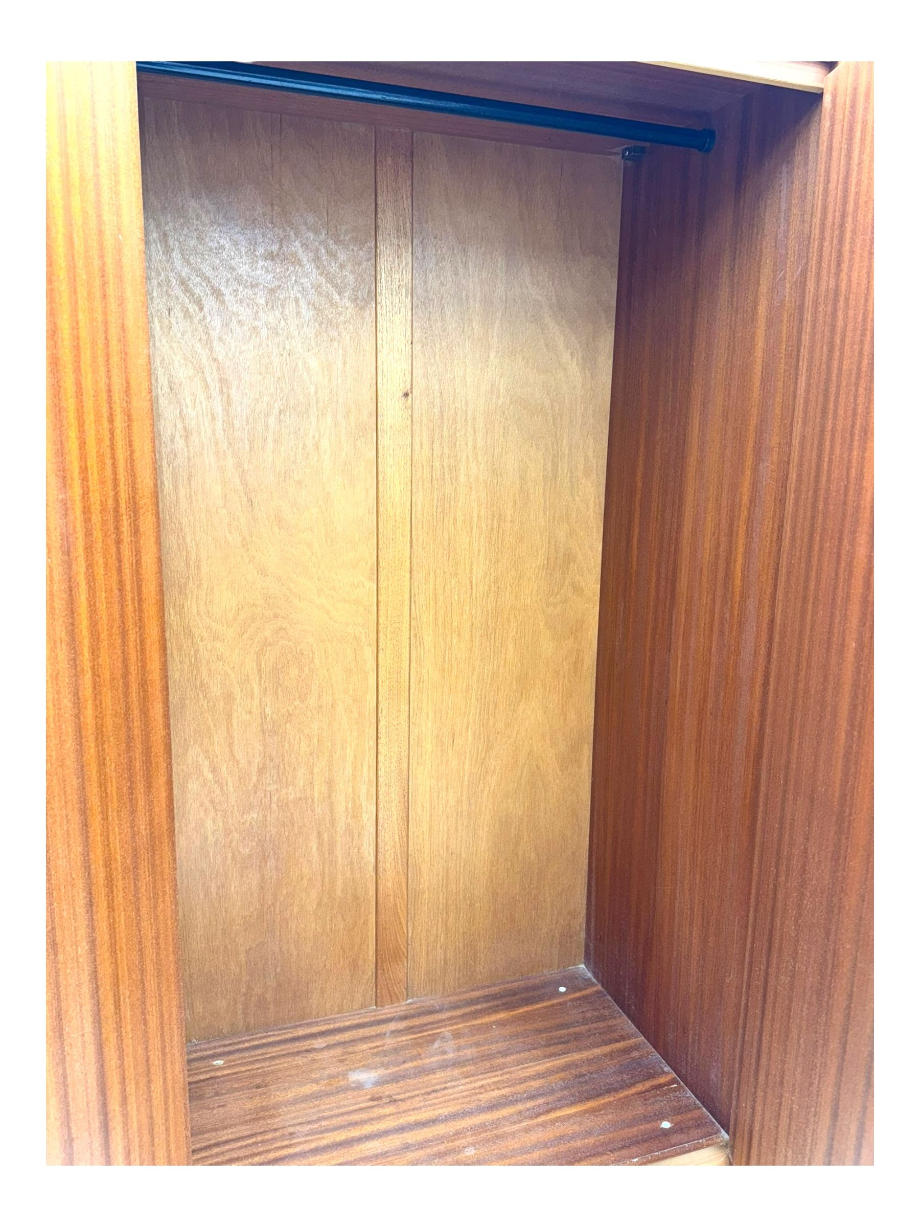 William Lawrence - mid-20th century teak double wardrobe, upper storage section over twin doors featuring recessed handles and contrasting horizontal panel, enclosing a hanging rail compartment, on plinth base with concealed castors
