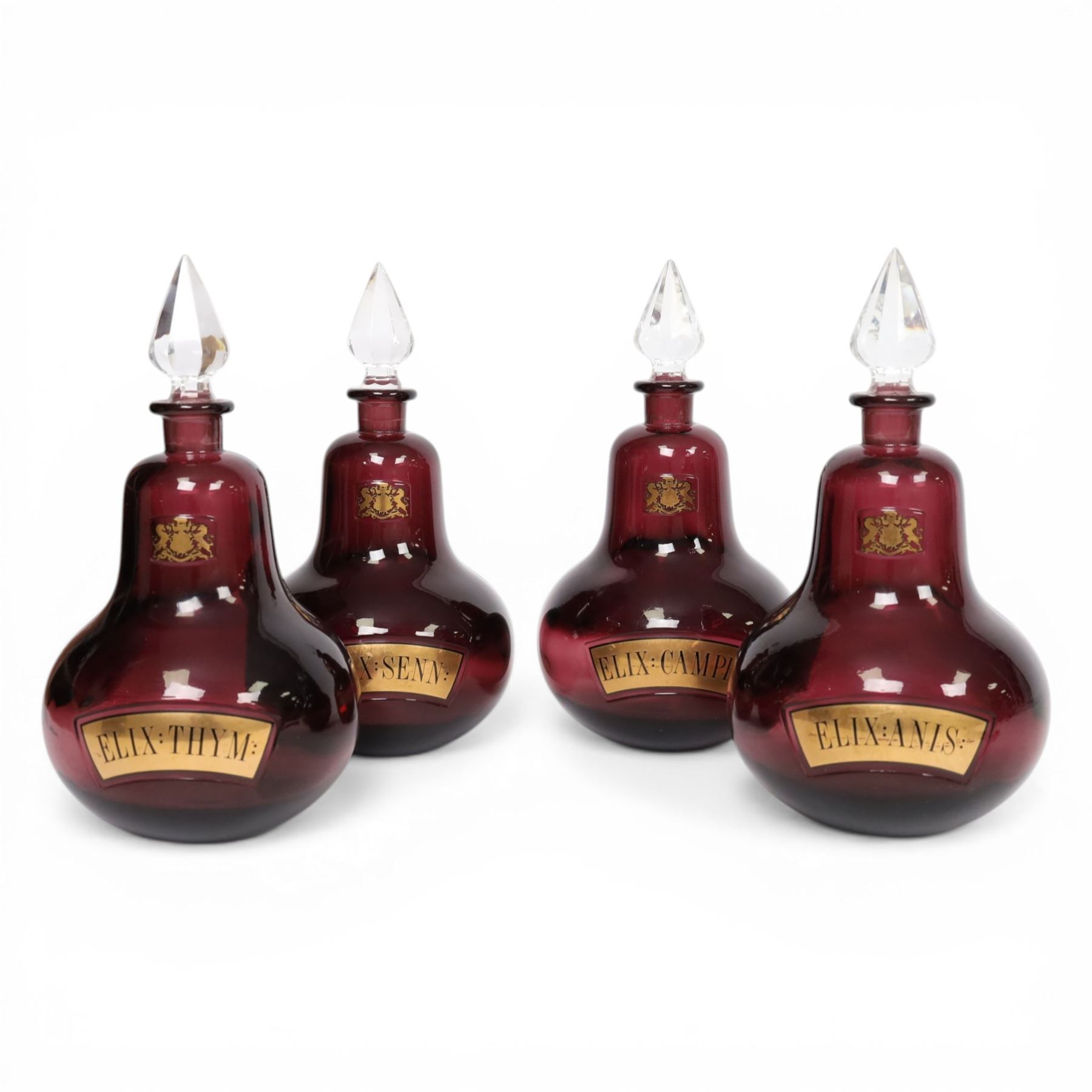 Set of four 20th century Royal Pharmaceutical Society amethyst glass bottles, of bellied form with clear cut glass spire stopper, each body bearing gilt label in Latin: ELIX:THYM:, ELIX:CAMPH:, ELIX:ANIS: and ELIX:SENN:, and gilt Royal Pharmaceutical Society crest to neck, H25cm

Provenance: From the collection of the family of Peter Green, a practising pharmacist whose career spanned the mid to late 20th century. During his professional life he managed pharmacies in Yeovil, Somerset, and later Selles Chemist in Filey, North Yorkshire, before purchasing and running his own business, Peter Green Pharmacy, located in the Market Place, Malton. The bottles were displayed as part of the traditional shop fittings in both the Filey and Malton pharmacies and were retained as part of his collection.