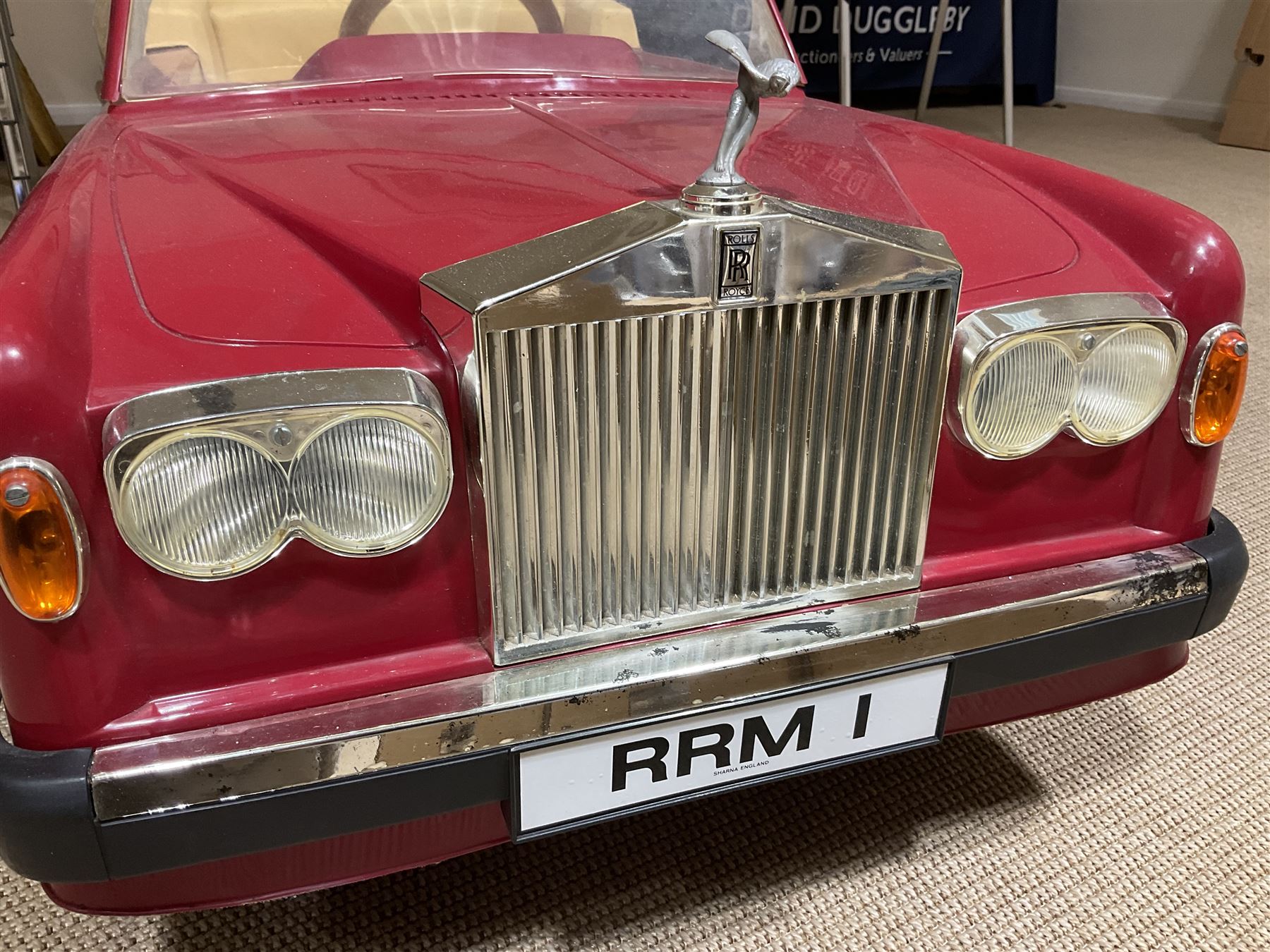 Early 1980s Rolls-Royce Corniche 'pedal' car by Sharna Tri-ang Limited, registration no.RRM1, steel chassis with treadle pedals, red moulded plastic body with flexible plastic 'Spirit of Ecstasy' car mascot on the radiator cap, opening boot lid, dashboard with decals of faux wood panelling and gauges, battery powered working electric lights, Sharna 235/70HR15 wheels with Rolls Royce hub caps, L123cm; together with two keys on RR fob, instructions manual in wallet, date stamped 17 November 1983, toy road tax disc dated 31.01.83/84 and original battery charger. 
Auctioneers Note: In 1983 Sharna Tri-ang Ltd., based at Lumb Mill in Droylsden, Manchester, took over from Tri-ang Toys at Merthyr Tydfil. They went on to launch a new range of toys based on children's TV programs, such as Knight Rider, Street Hawk, Roland Rat, The A-Team, The Get A-Long Gang and Postman Pat, as well as Rolls-Royce Corniche pedal cars, which were available in red, white or blue. 