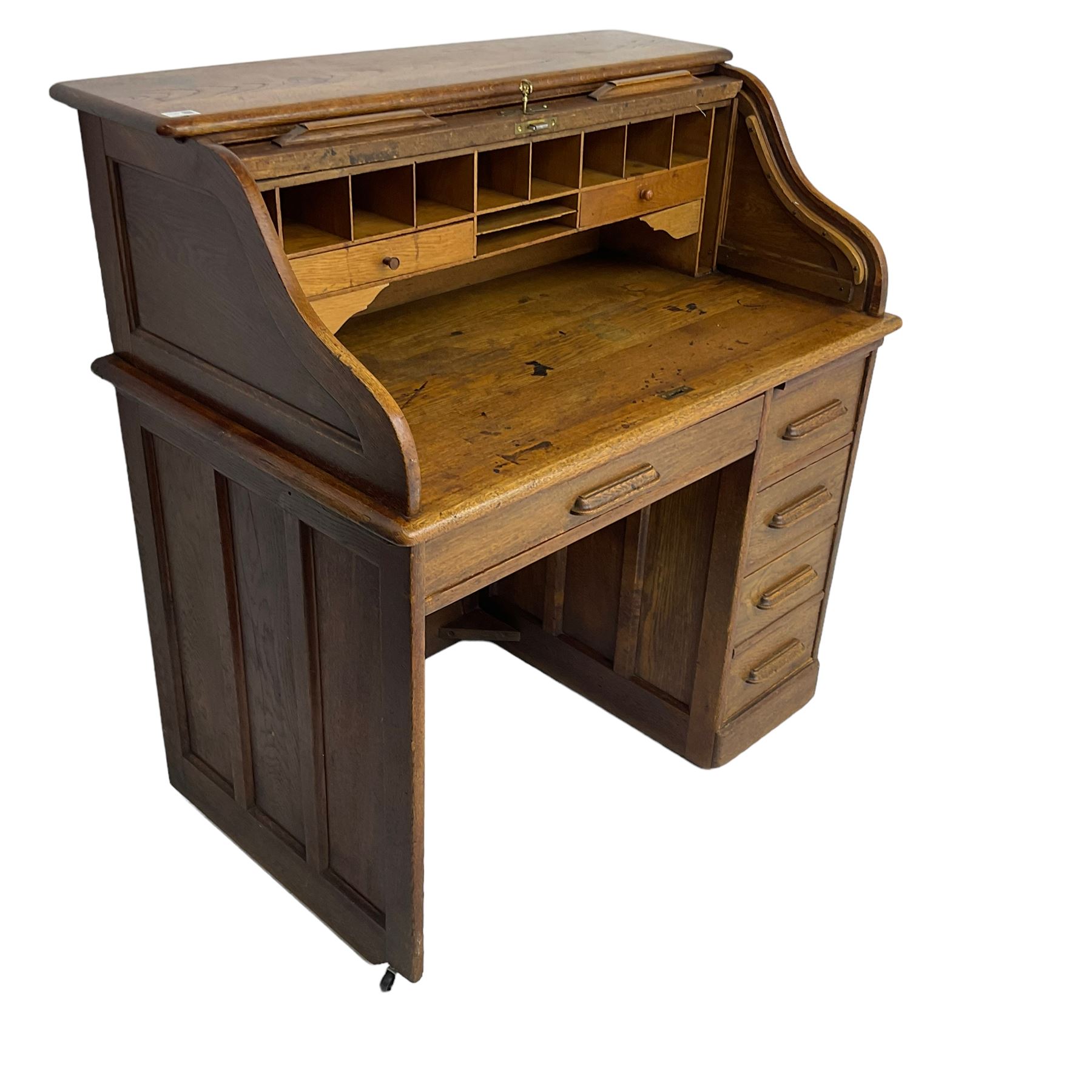 Early 20th century oak roll-top desk, the tambour enclosing pigeon holes and small drawers, the base fitted with slide, a single long drawer and three smaller drawers