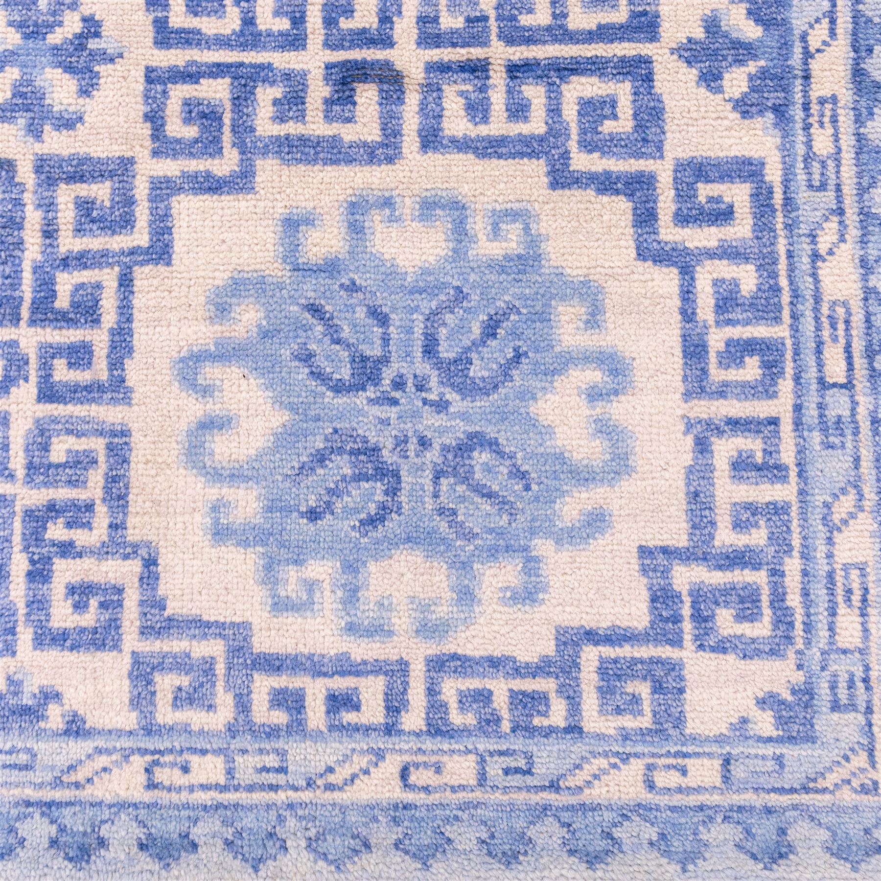 Late 20th century Chinese hand-woven wool carpet, ivory field with a lattice of stylized lotus medallions, contained within geometric key fret panels interspersed with a small floral device enclosed within a complementary Greek-Key border, the designs in tones of pale blue and soft cream