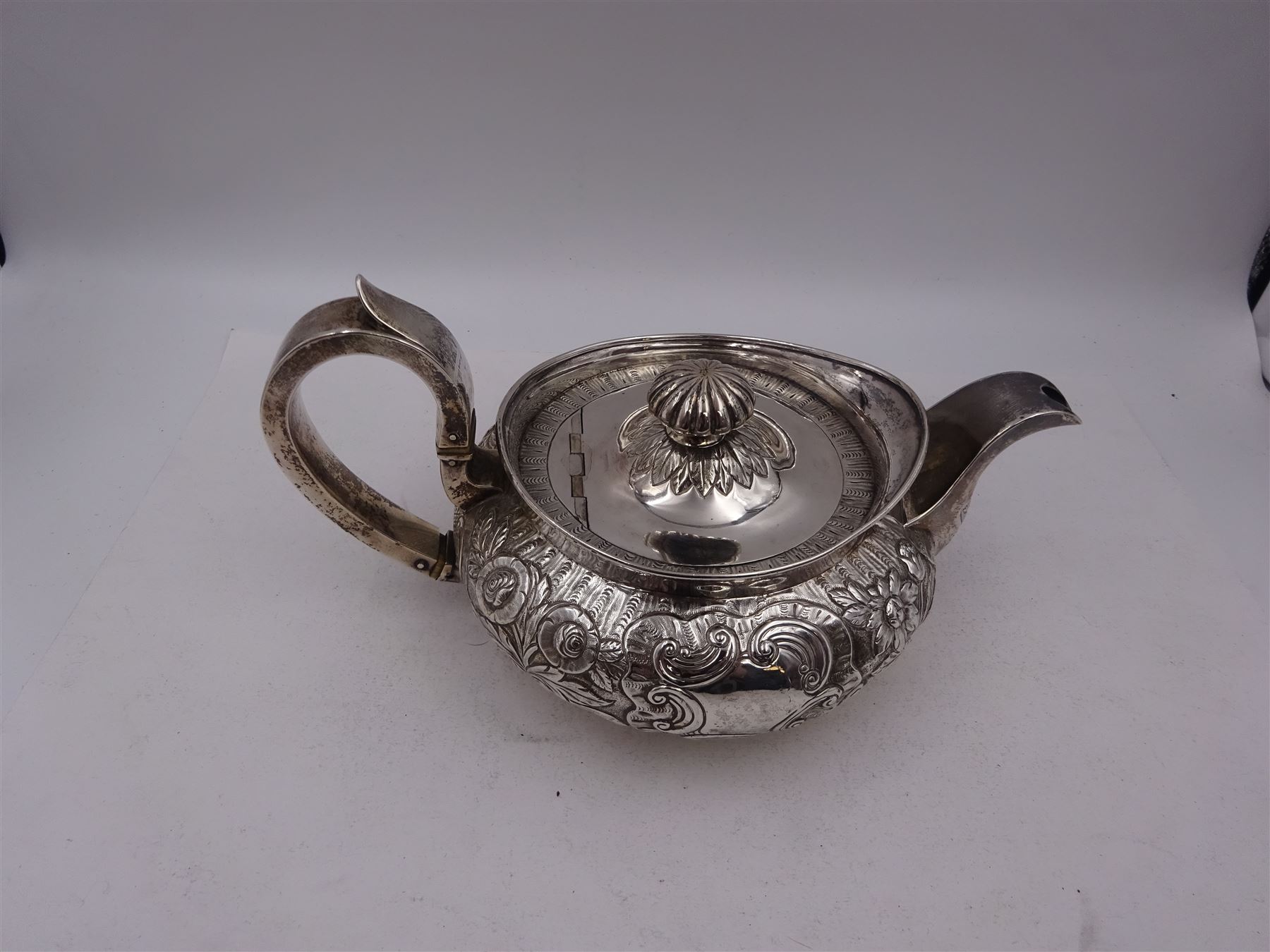 George III Irish silver teapot, of squat circular form, the body with repousse and chased floral and C scroll decoration, with capped C handle and ivory insulators, engraved to base 'Presented to Troop Sergeant Major John Percival, of the 4th Dragoon Guards by Alex D. Tait, Esq, late Captain in that corps as a mark of approbation of his steady and upright conduct when Sergeant Major of his Troop, Dublin, June 2nd 1843', hallmarked William Law, Dublin 1817, H12.5cm, This item has been registered for sale under Section 10 of the APHA Ivory Act