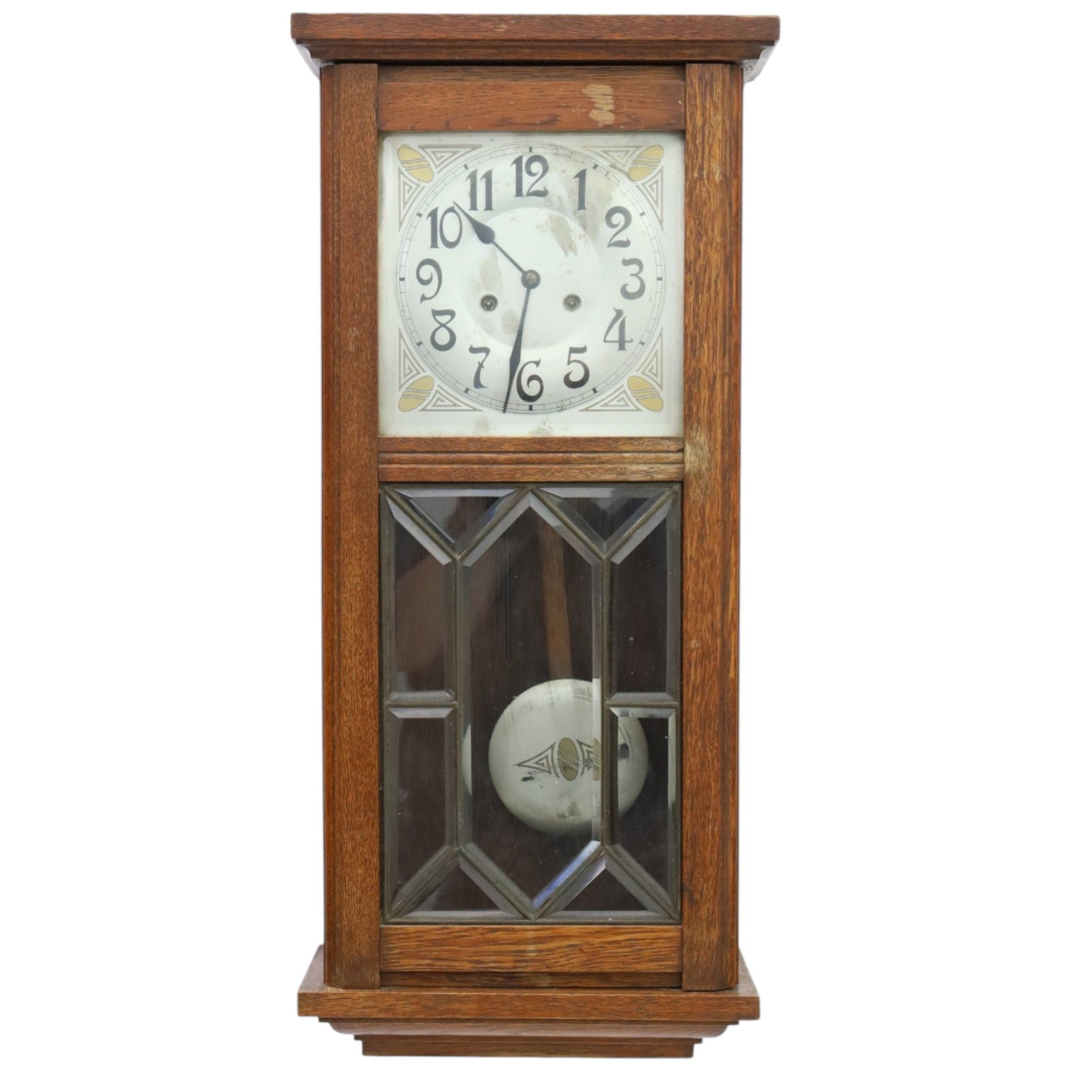 Art Deco style oak wall clock, moulded cornice above a silvered dial with Arabic numerals and geometric spandrels, glazed door with geometric bevelled glass panels enclosing a circular pendulum, on a stepped moulded base