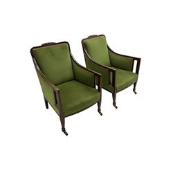 Pair Edwardian mahogany framed armchairs, with satinwood stringing, foliate carved cresting rail, upholstered in green fabric with sprung seat, raised on square tapering supports with spade feet and brass castors