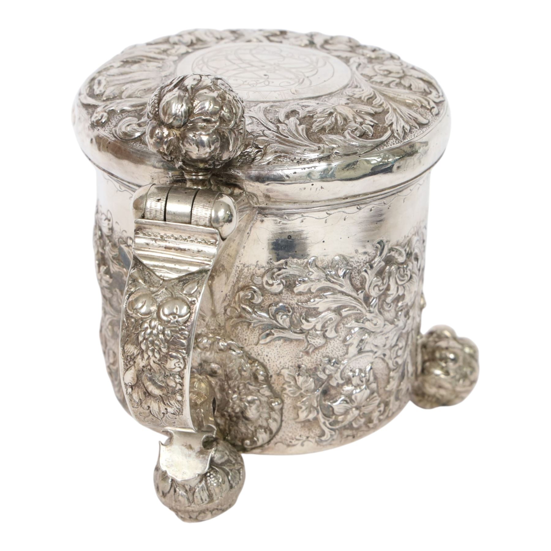 Northern European silver peg tankard, probably late 18th/early 19th century, of cylindrical form, the body repoussé decorated with scrolling and blossoming acanthus, fitted with scroll handle with shield terminal, the hinged cover with conforming repoussé decoration surrounding a central circular panel engraved with monogram beneath initials EASBGD, opening with ball thumbpiece detailed with fruits, raised upon three confirming ball feet mounted with shaped panels also detailed with fruits, bearing indistinct mark beneath, H19cm