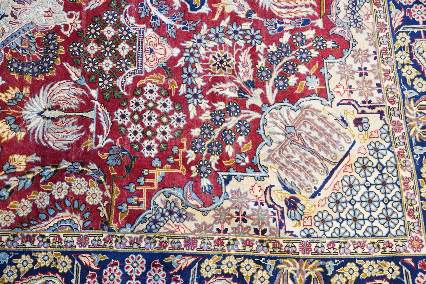 Central Persian Najafabad hand-knotted carpet, crimson field with a central elaborate cusped medallion with radiating floral motifs, surrounded by finely drawn scrolling vines incorporating stylized palmettes and rosettes, flowering plants and vase motifs, ivory spandrels similarly decorated enclosed by a dark indigo main border of floral arabesques between multiple guard stripes, with cotton fringe ends 