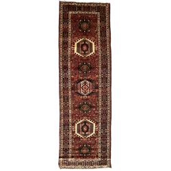 Persian Karajeh red ground runner, the field set with seven trailing geometric medallions, the field decorated all over with stylised plant motifs, the multiple banded border with repeating geometric flower head patterns